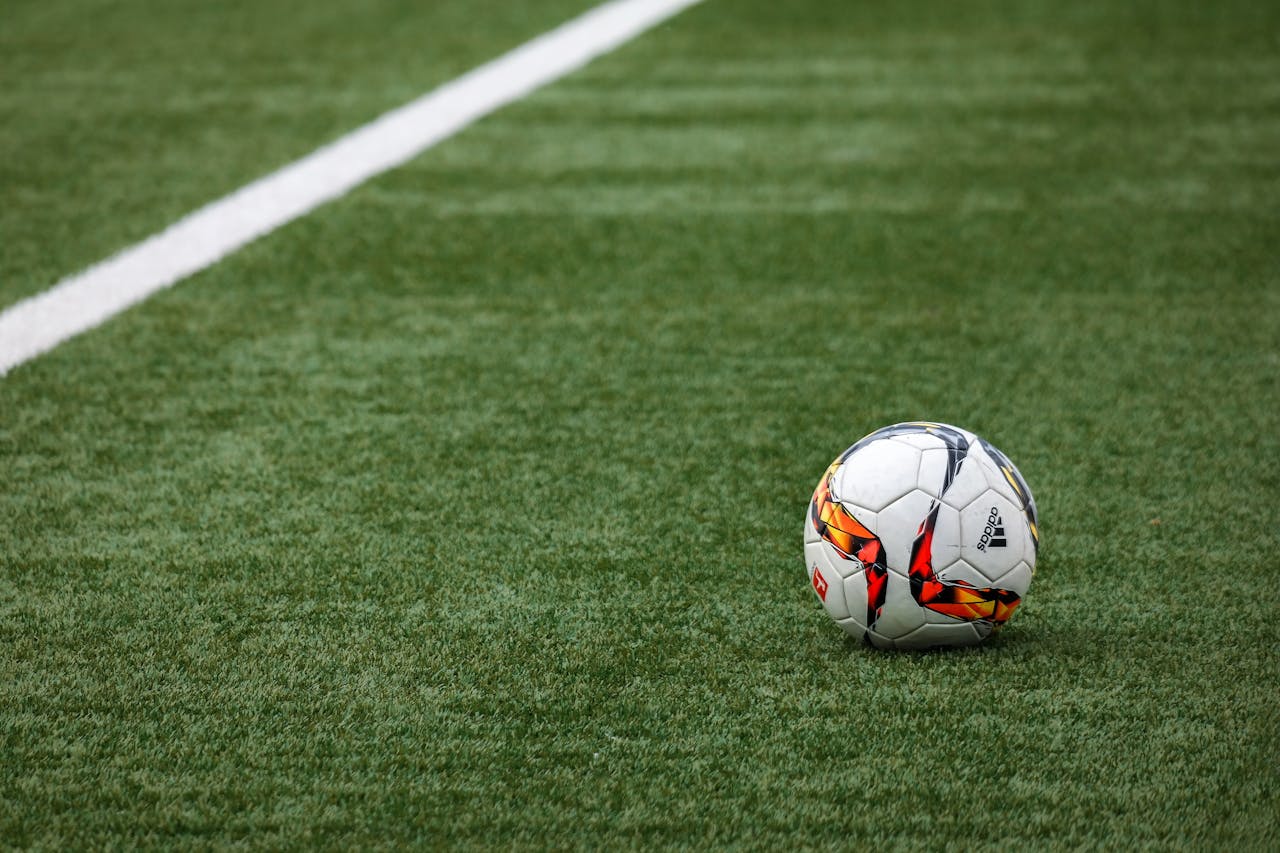 services-03 A vibrant soccer ball resting on a pristine grass field beside a white sideline.